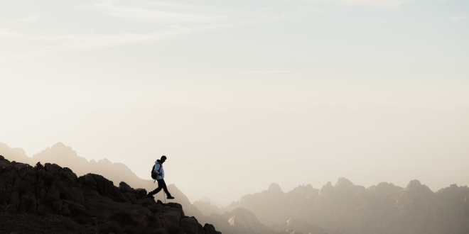 a man running up a mountain with a sky background